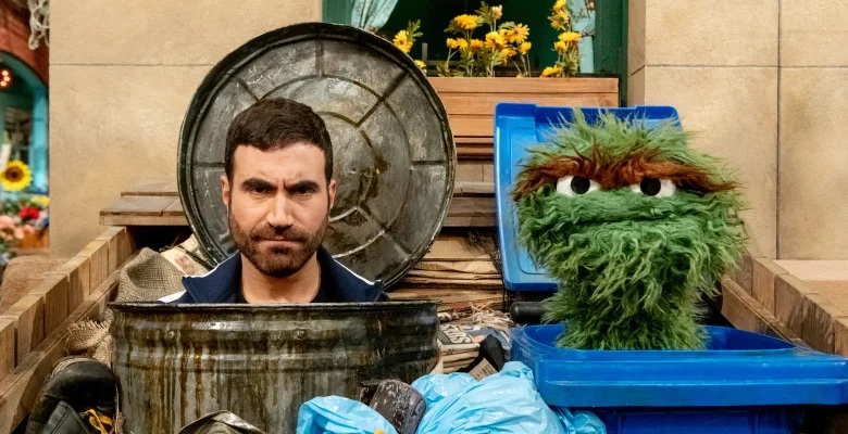 Actor Brett Goldstein and Oscar the Grouch peer out from trash cans.