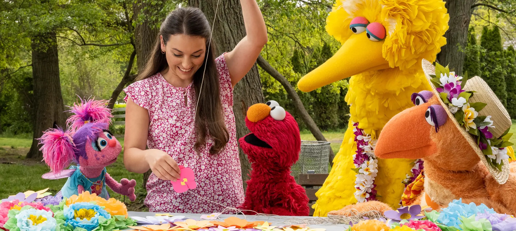 A woman makes paper flowers with Abby, Elmo, and Big Bird.