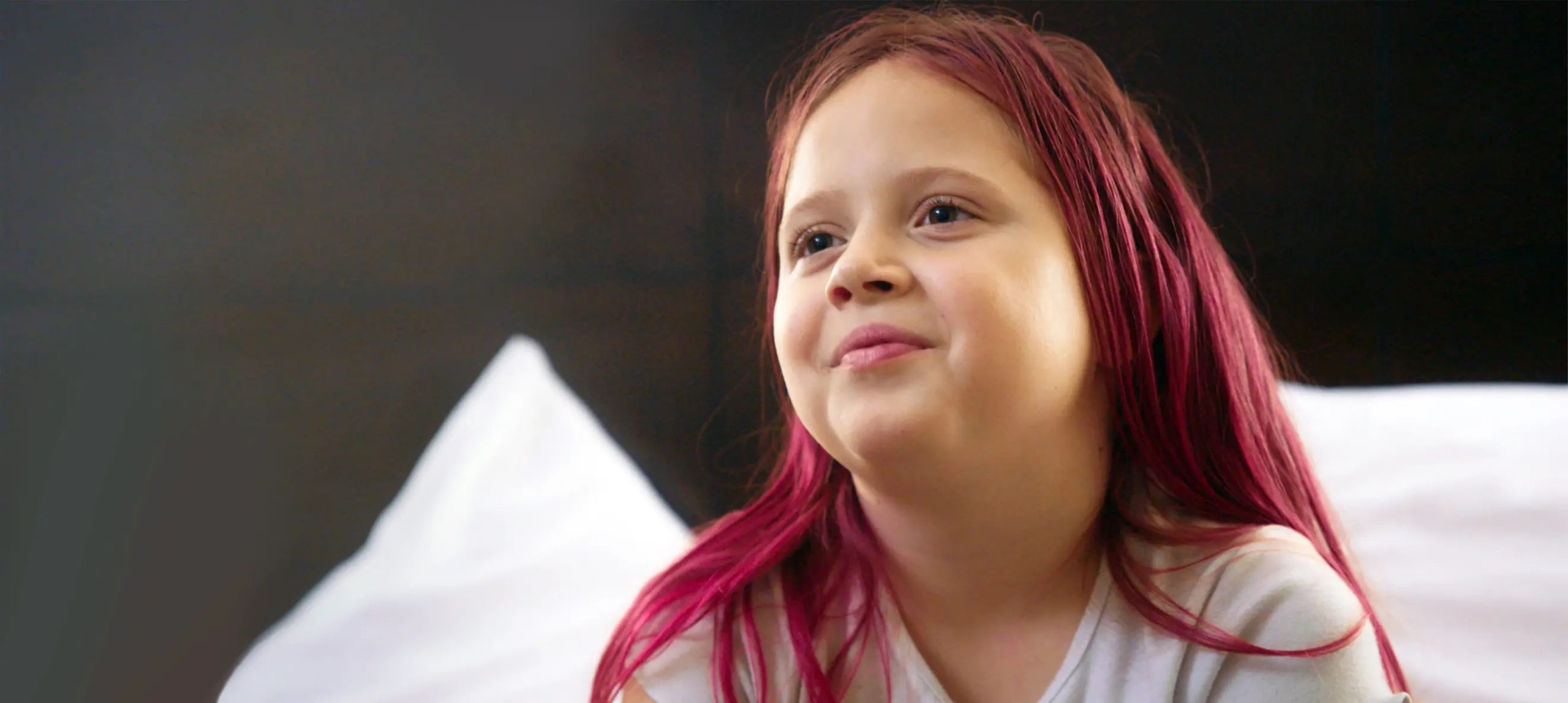 A young girl with red hair smiles and looks up and in the distance.