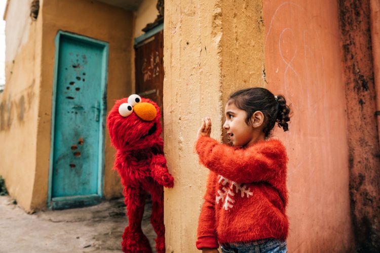 Elmo and a young girl play hide and seek.