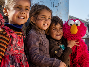 Children hugging Elmo outside.