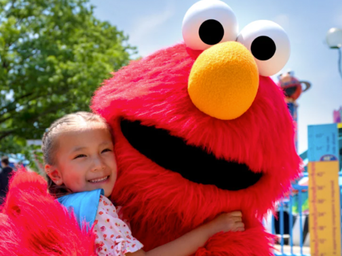 Theme park Elmo hugging a child.