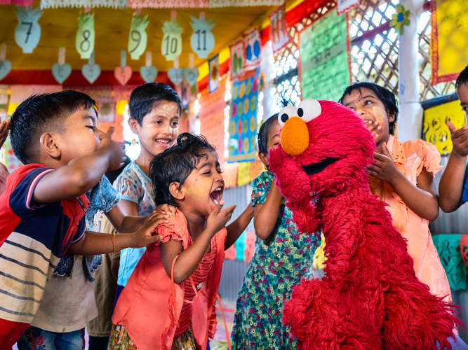 Elmo laughing with a group of children.