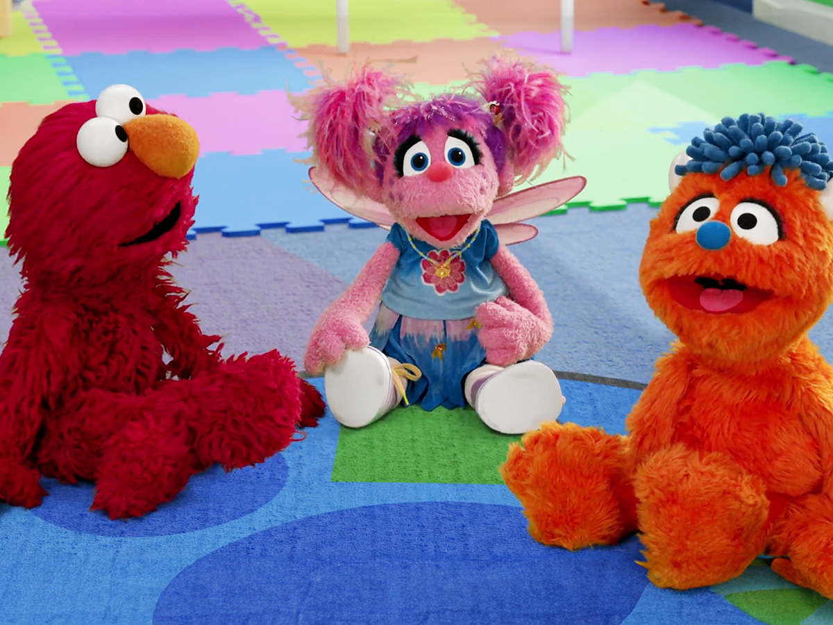 Elmo, Abby and Rudy sitting on a rug.