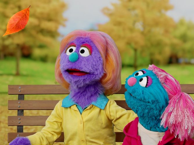 An adult Muppet sits with a younger Muppet on a park bench