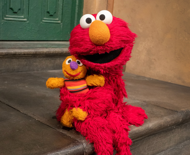 Elmo sits on the stoop of 123 with Baby David