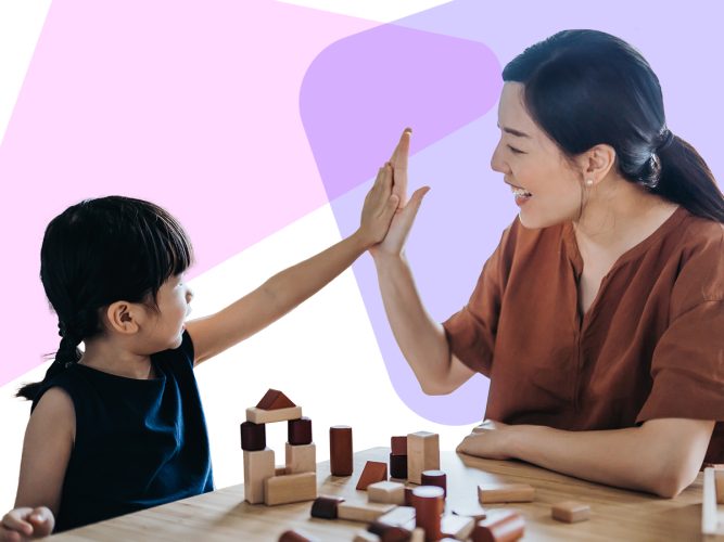 A caregiver and a child high five next to a tower of blocks