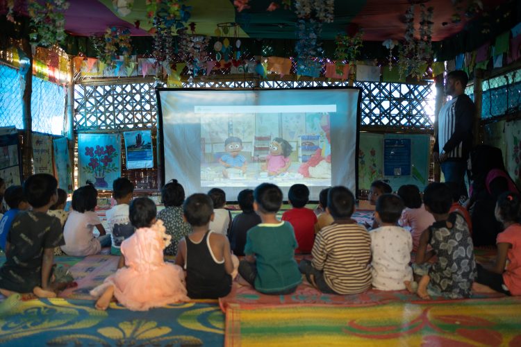 Children watching a projector with Sesame Street on it.