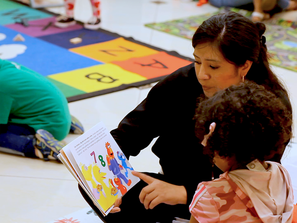 A teacher reading to a child on a mat in a classroom.