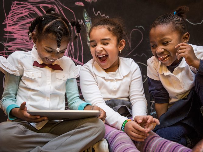 Children laughing while looking at a tablet.