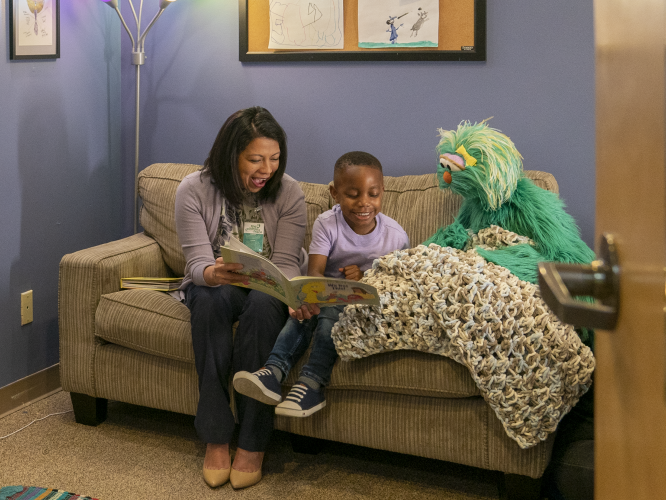 A parent and child sitting with Rosita on a couch.