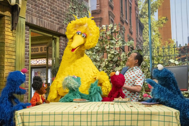 The Muppets and Alan standing around a table.