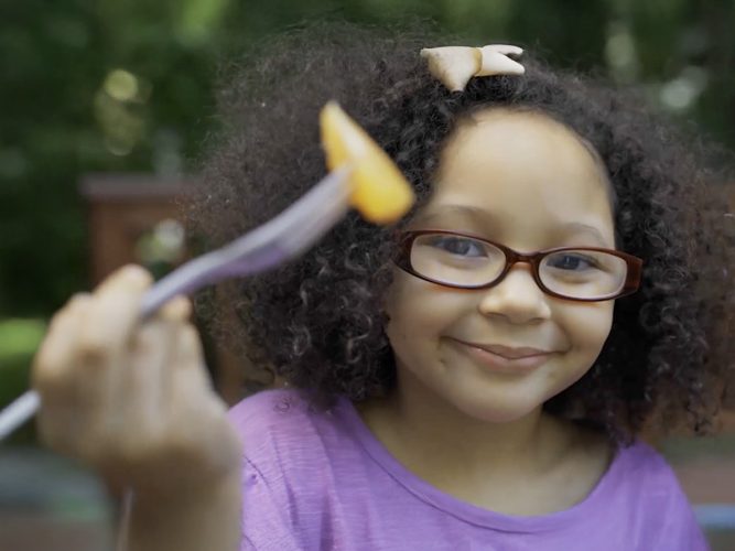 A child holding a piece of fruit on a fork.
