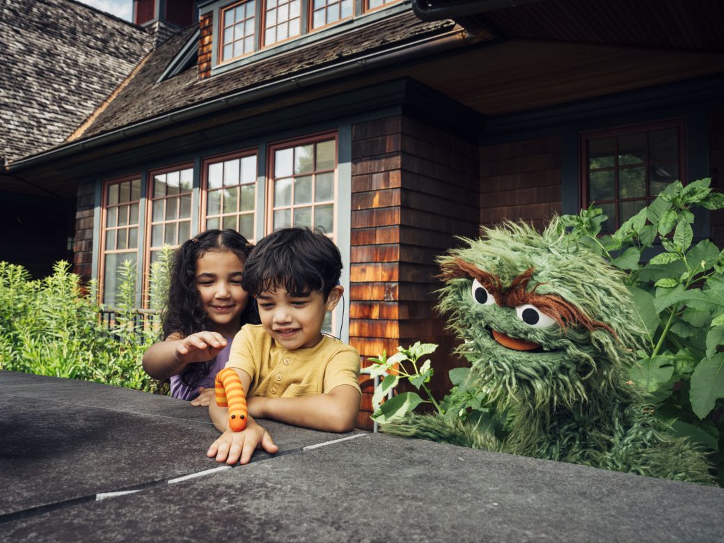 Oscar the Grouch playing with two children outside.