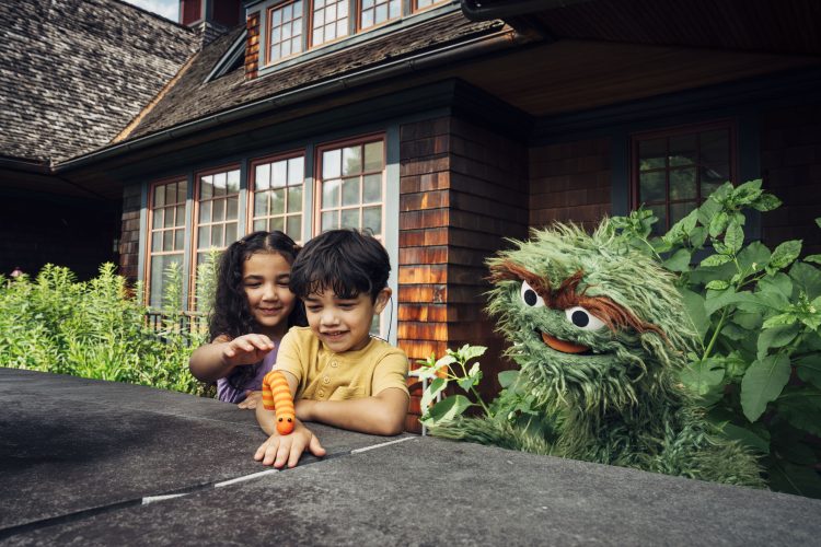 Oscar the Grouch playing with two children outside.